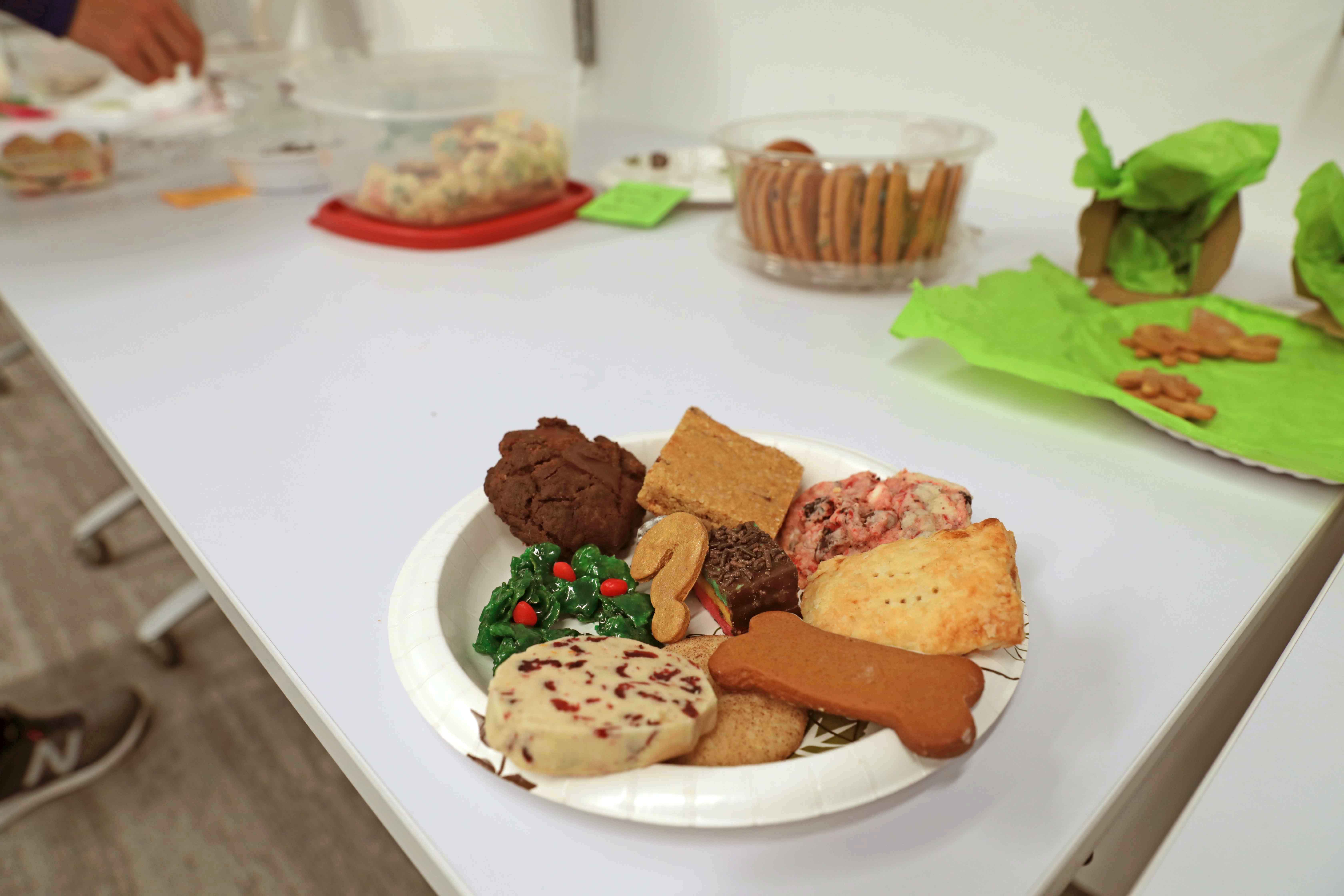 A plate of cookies on a table, with containers of cookies in the background